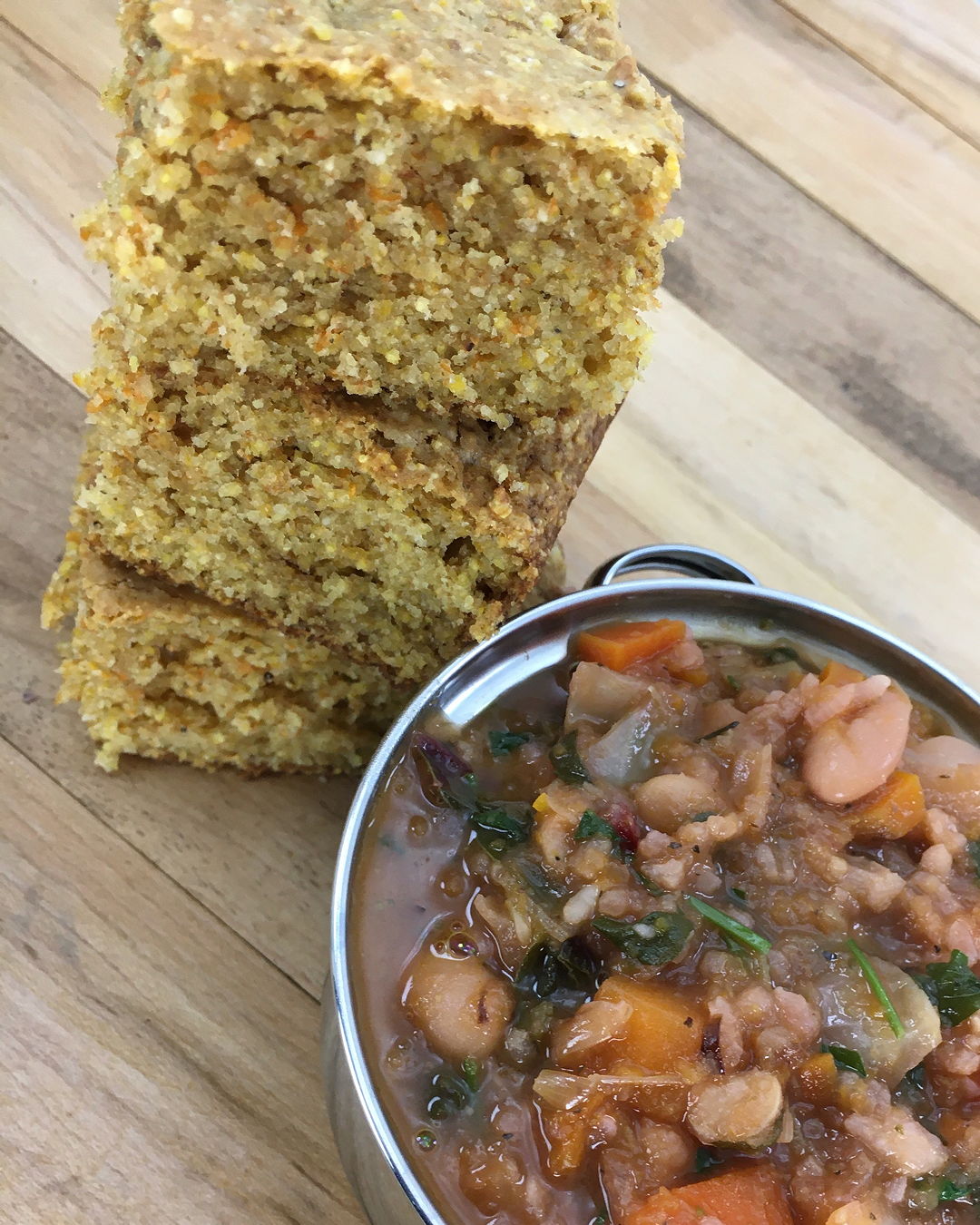 three pieces of cornbread piled atop each other and next to a small tureen of minestrone soup